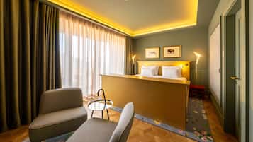 A hotel room with a bed, a desk, a chair, a small table, and a door.