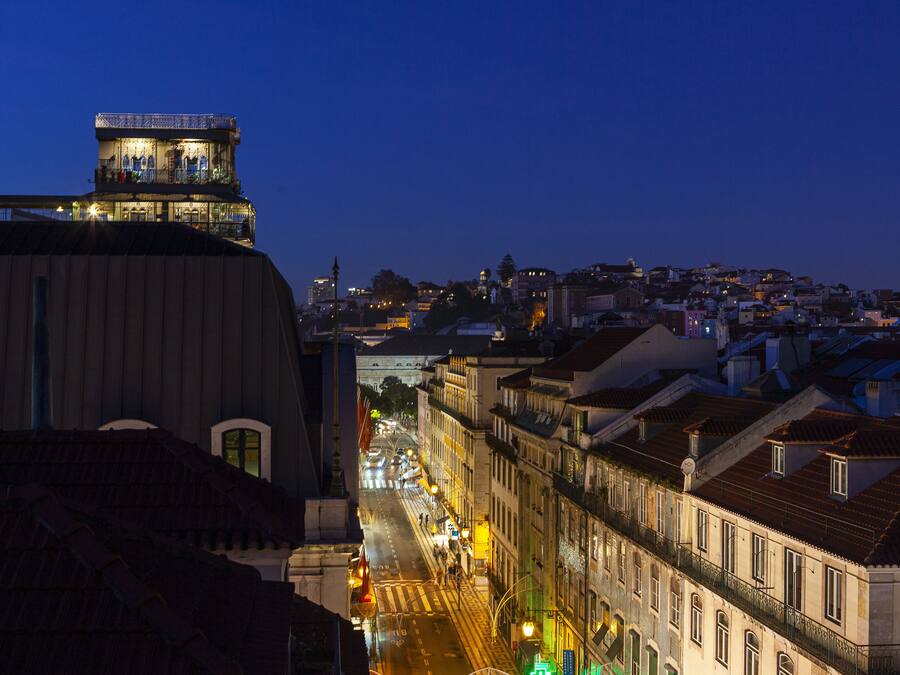 A cityscape at dusk with illuminated buildings and a prominent tower.