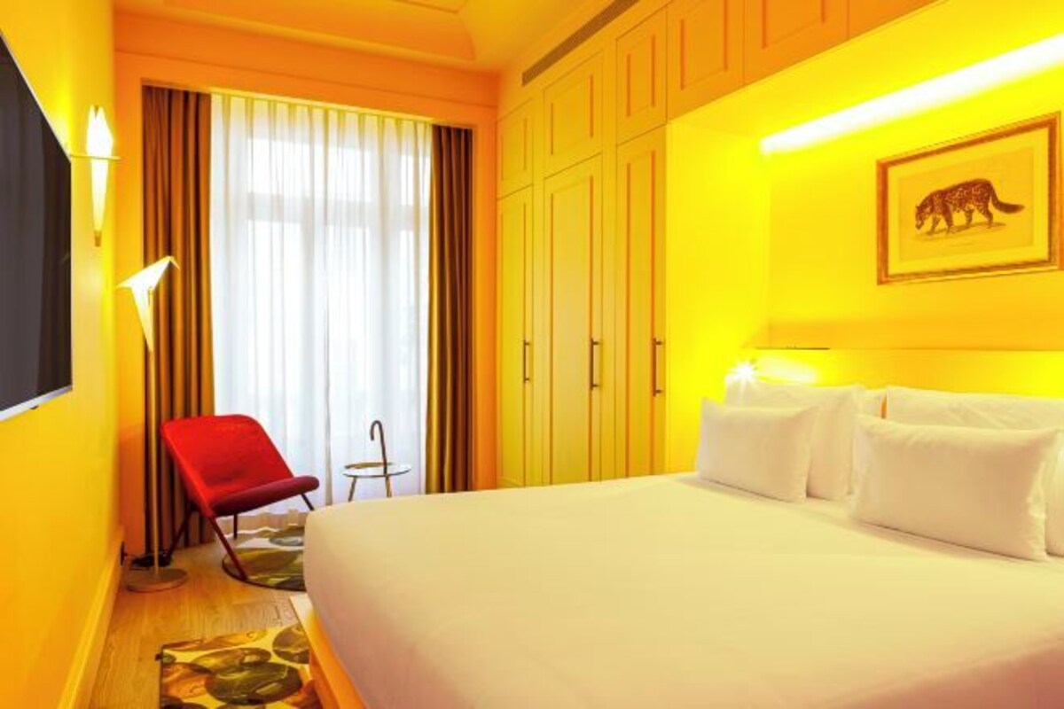Una habitación de hotel con una cama grande, una silla roja, una mesita pequeña y un armario.