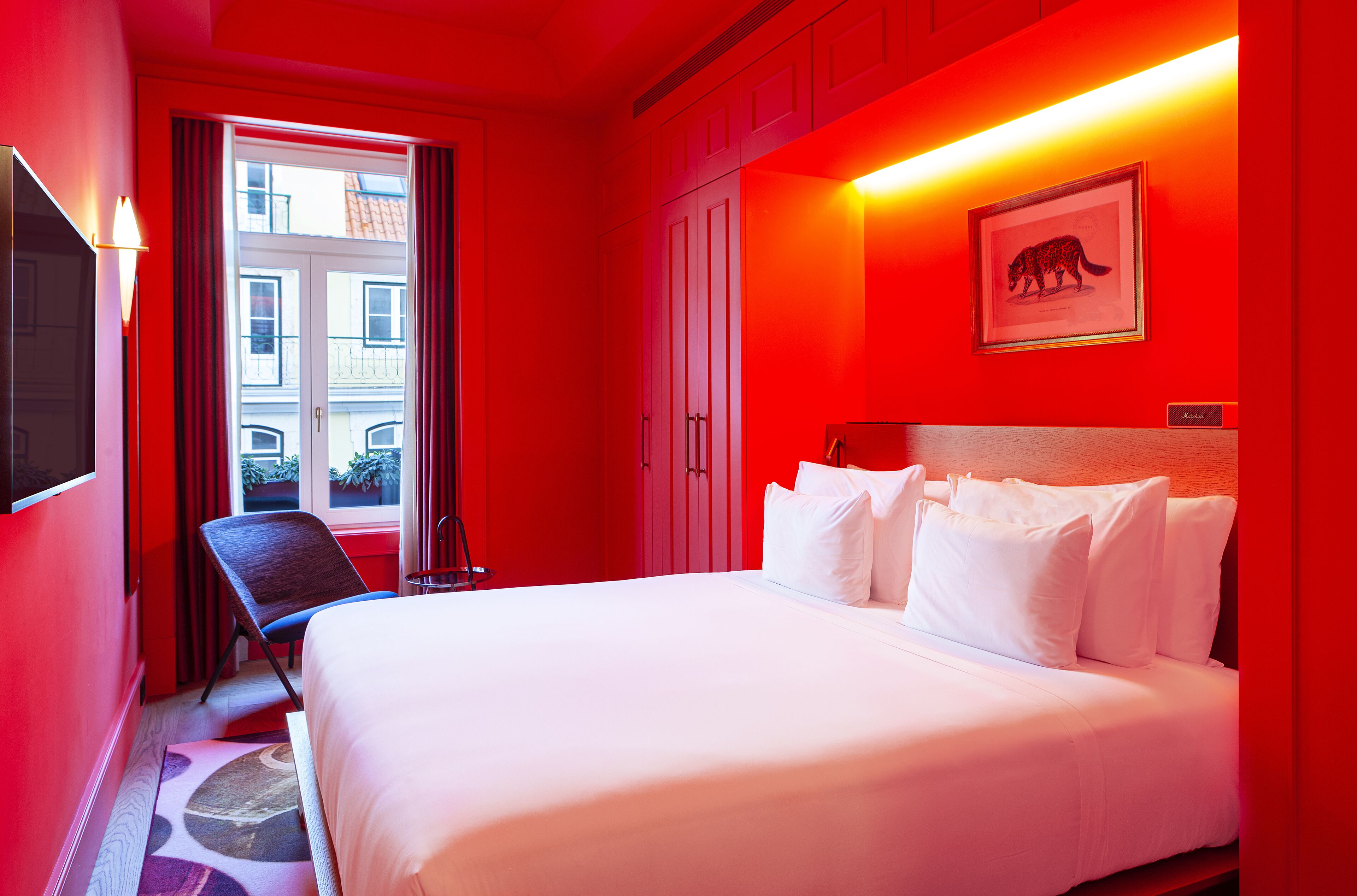 A hotel room with a bed, a chair, a desk, and a window with curtains.