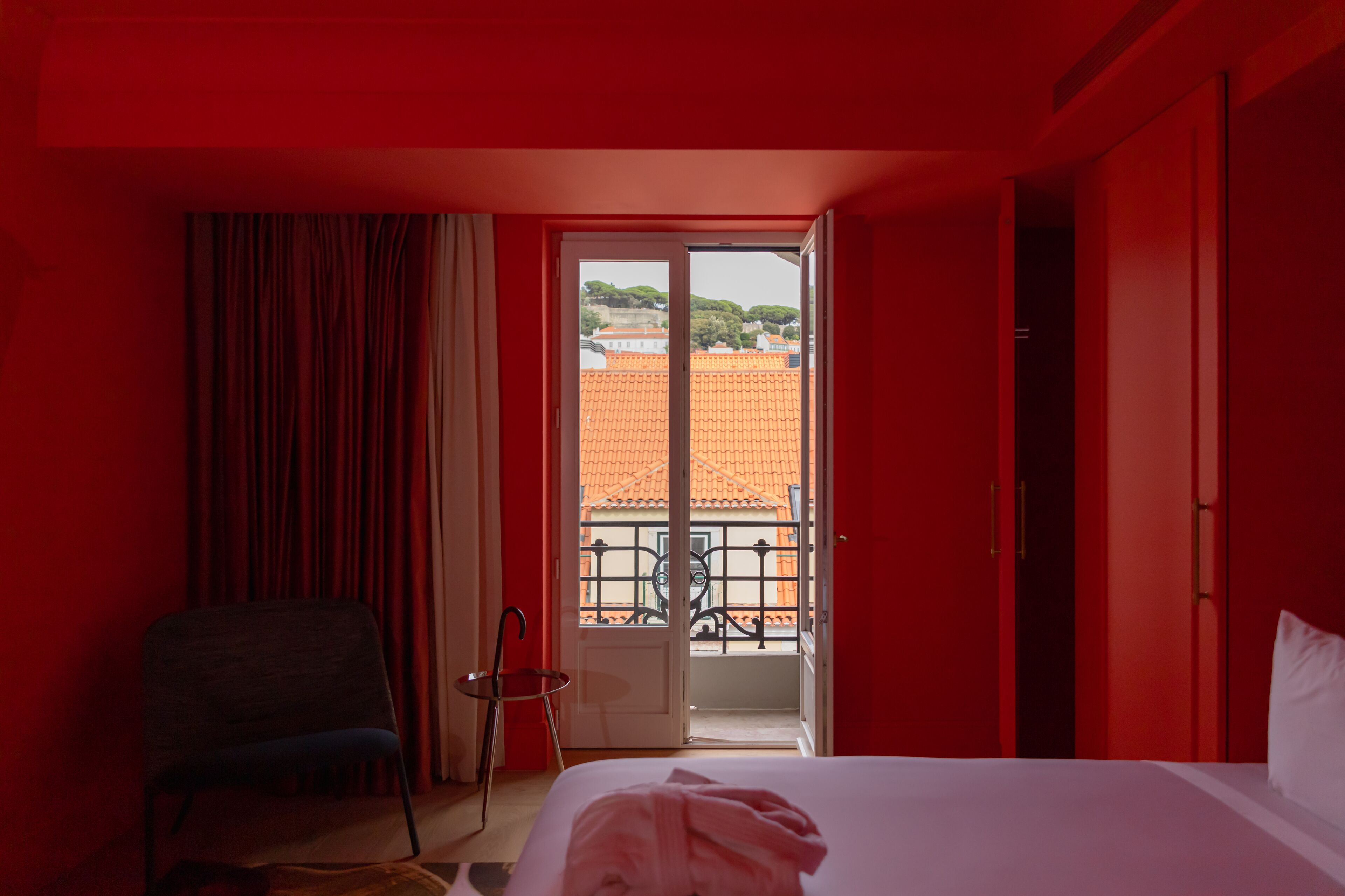Una habitación de hotel con cama, una silla, una ventana con vista a edificios y una puerta.
