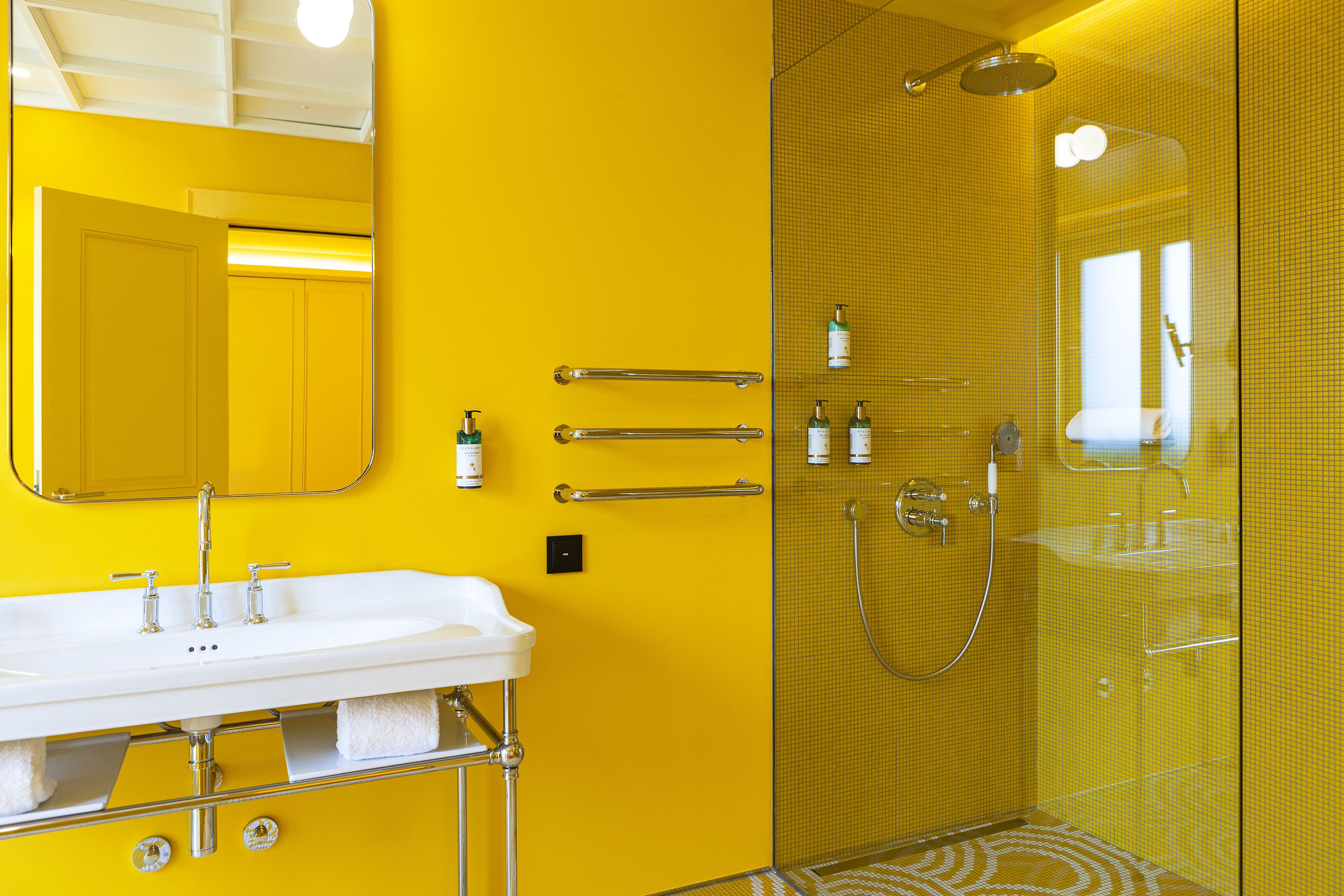 Un bagno con una parete gialla, un lavandino bianco, una cabina doccia in vetro e uno specchio sopra il lavandino.