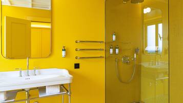 Un bagno con una parete gialla, un lavandino bianco, una cabina doccia in vetro e uno specchio sopra il lavandino.