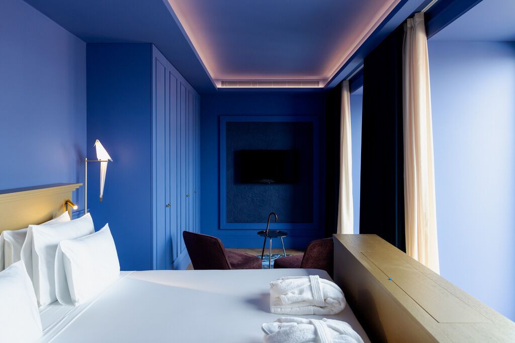 A hotel room with a bed, a desk, a chair, a TV, and a window with curtains.