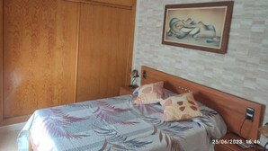 A bedroom with a bed, wooden wardrobe, ceiling fan, and a painting on the wall. - Apartamento Villa Inés (Huércal de Almería)