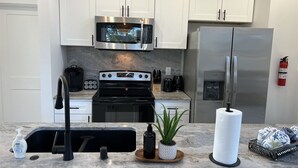 A modern kitchen with white cabinets, stainless steel appliances, a built-in microwave, a refrigerator, and a sink with a faucet. - Drift Inn Duplex B - with hot tub (Ocean Shores)