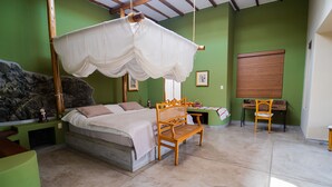 A bedroom with a bed, a wooden chair, a nightstand, a green wall, a window, and a stone wall. - Andenes de Azpitia (Santa Cruz de Flores)