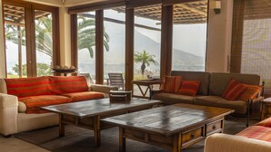 A spacious living area with two sofas, a coffee table, and a view of palm trees and mountains through large windows. - Andenes de Azpitia (Santa Cruz de Flores)