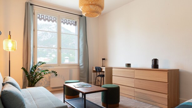 Een moderne woonkamer met een bank, een klein tafeltje, een kast en een raam met gordijnen.