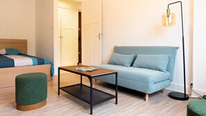 Een moderne slaapkamer met een bed, een blauwe bank, een klein houten tafeltje en een groene poef.