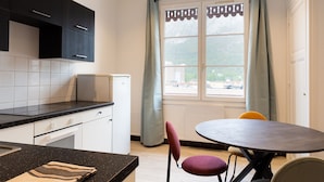 Een kleine keuken met een koelkast, een eettafel met stoelen en een raam met gordijnen.