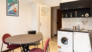 Een kleine keuken met een wasmachine, een eettafel met stoelen en een ingelijst kunstwerk aan de muur.