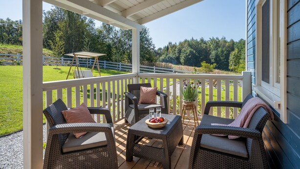 Un espace extérieur abrité avec des meubles en osier, une table garnie de fruits et une vue sur un champ verdoyant et des arbres.
