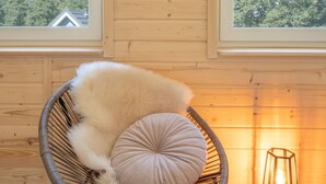 Un intérieur en bois agrémenté d’une œuvre d’art représentant une tête de cerf encadrée, d’un fauteuil en osier avec un coussin moelleux et d’une petite table sur laquelle est posée une lanterne.