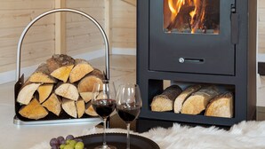 Un poêle à bois avec des bûches, une porte en verre et une grille métallique pour entreposer le bois de chauffage.