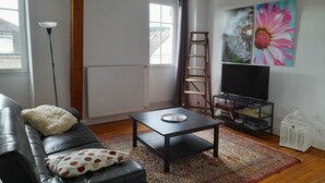 Ein Wohnzimmer mit einer schwarzen Ledersofa, einer Holzleiter, einem Fernseher auf einem Schrank und einem großen Blumenbild an der Wand.