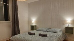 Ein Schlafzimmer mit einem Bett, zwei Nachttischen mit Lampen, einem Fenster mit Vorhängen und einem Holzboden.