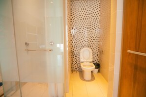 A modern bathroom with a glass shower enclosure, a toilet with a mosaic tile wall, and a wooden door. - Cozy studio suite at D majesti (Kuala Lumpur)