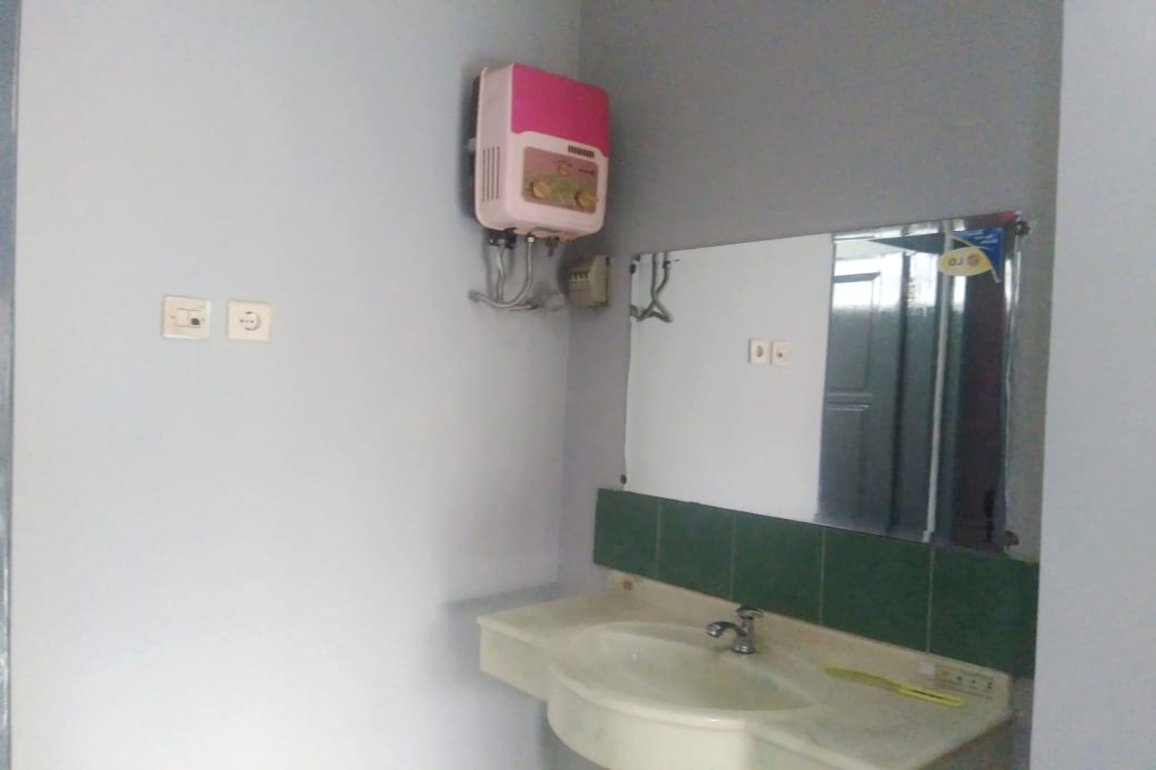 A bathroom with a sink, mirror, and a pink water heater mounted on the wall.