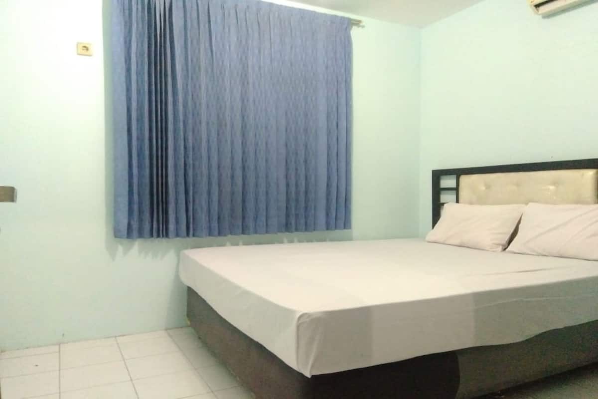 Un dormitorio con una cama, un ventanal con cortinas azules y una pared de tono claro.