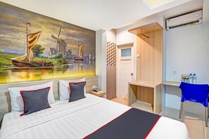 A hotel room with a bed, a painting of a sailboat, a wooden desk, a blue chair, and an air conditioning unit. - Hotel O Gardenia Boarding House (Purwokerto)