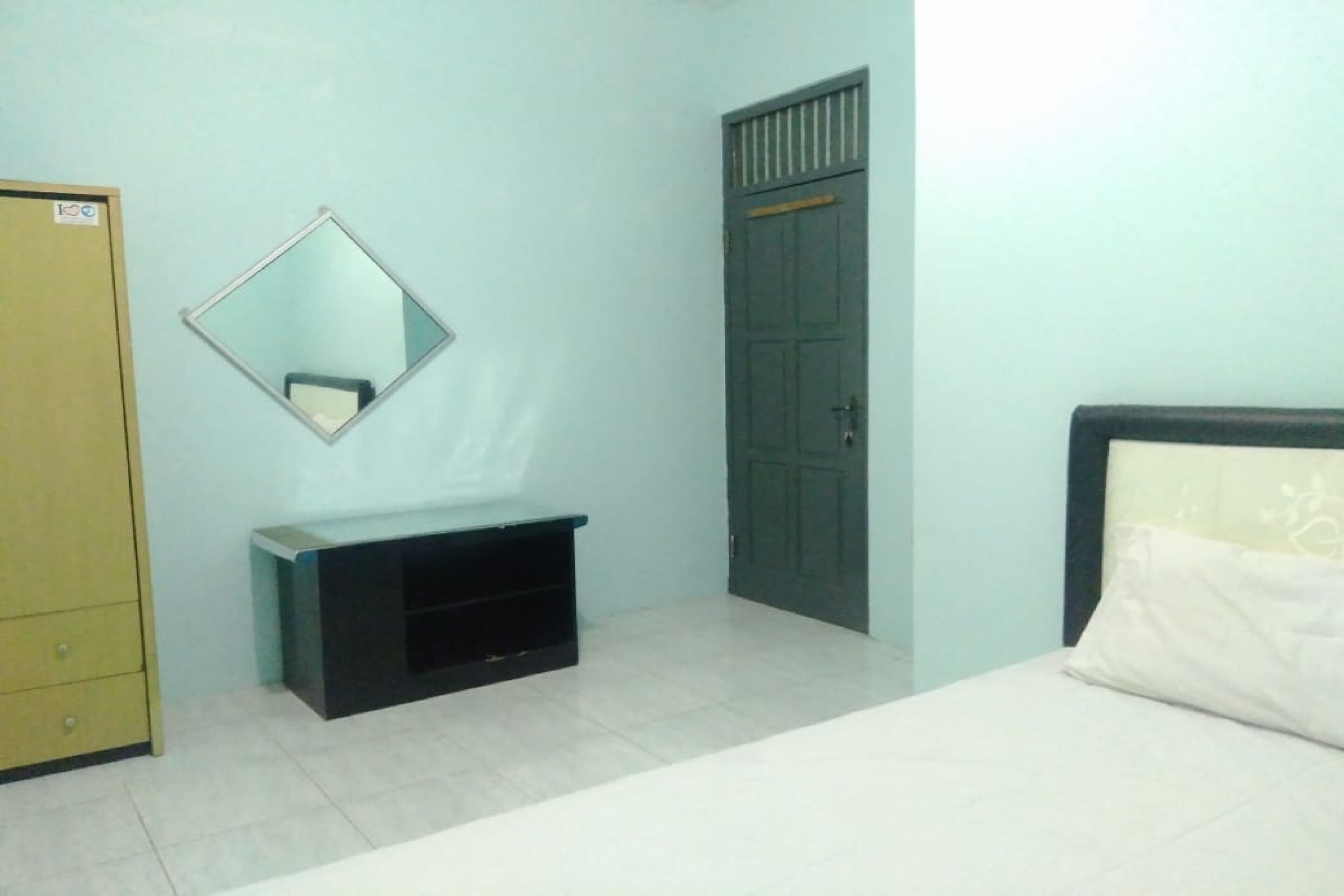 Una habitación con cama, armario, espejo y un pequeño mueble negro.