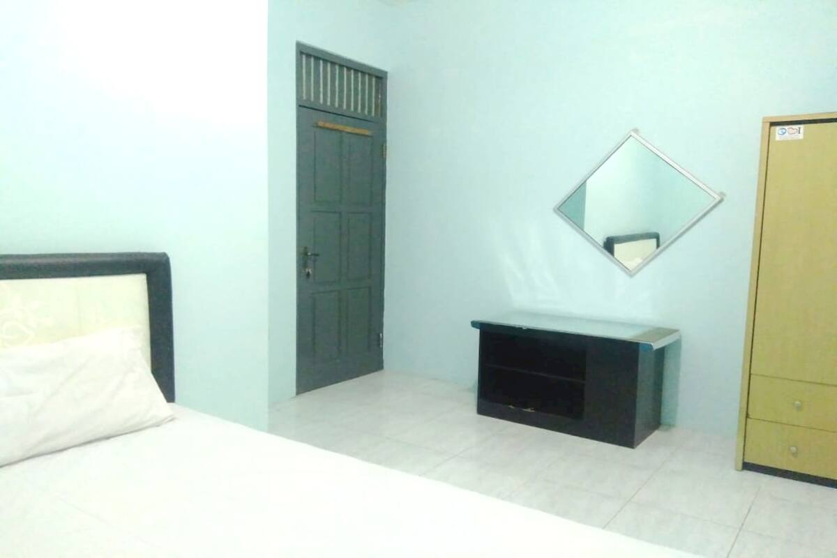 Un dormitorio con cama, armario, espejo y mueble para televisión.