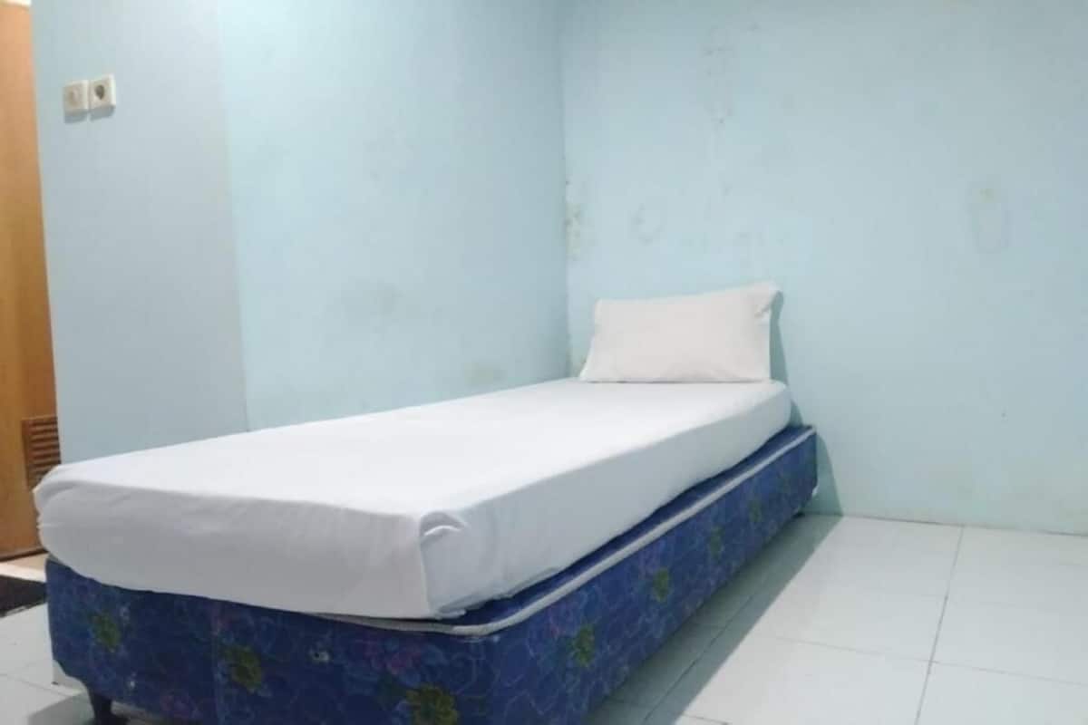 Una habitación pequeña con una cama individual, colchón azul y ropa de cama blanca.