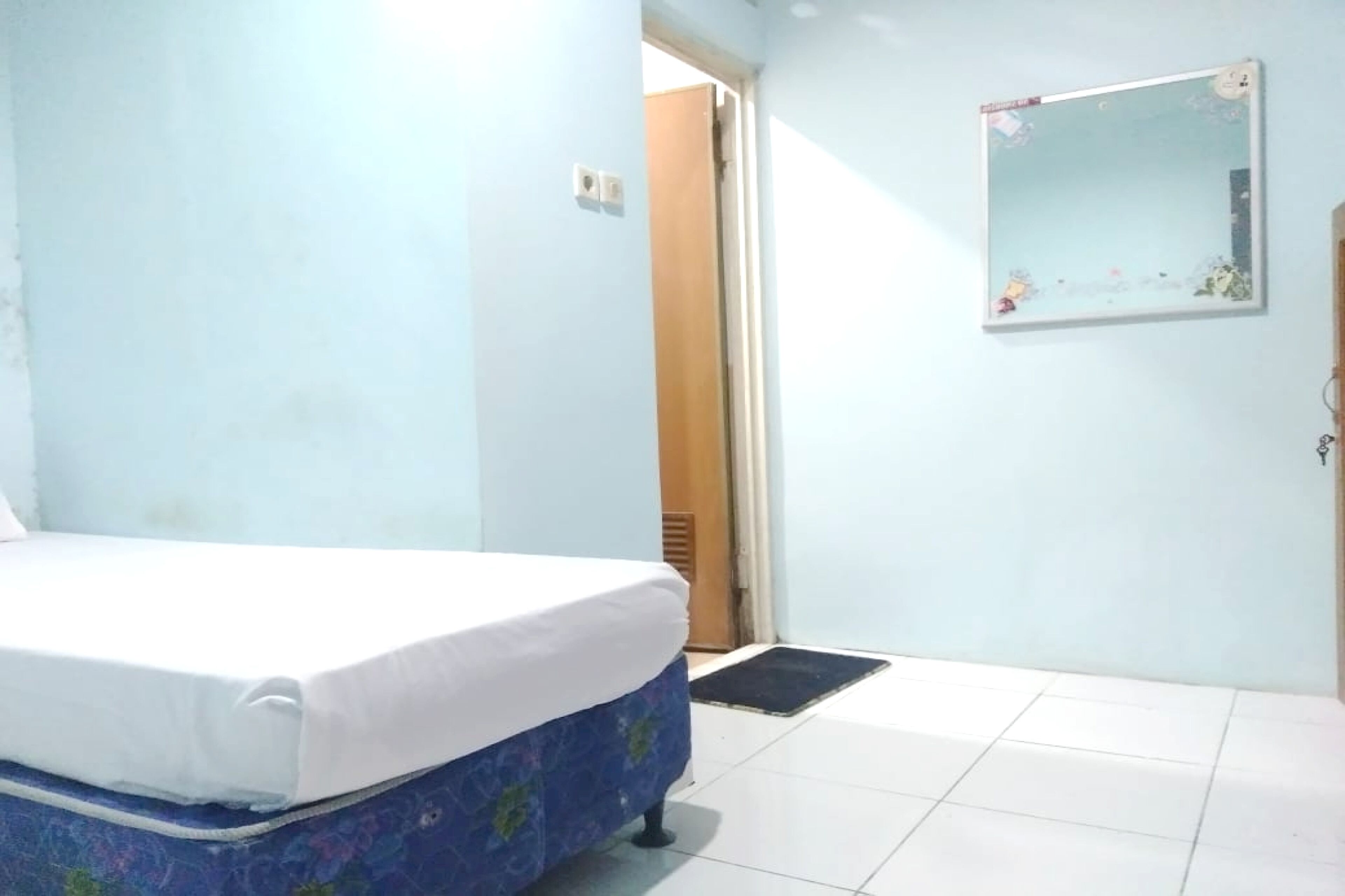Une chambre à coucher avec un lit, une porte, un miroir fixé au mur et un sol carrelé.