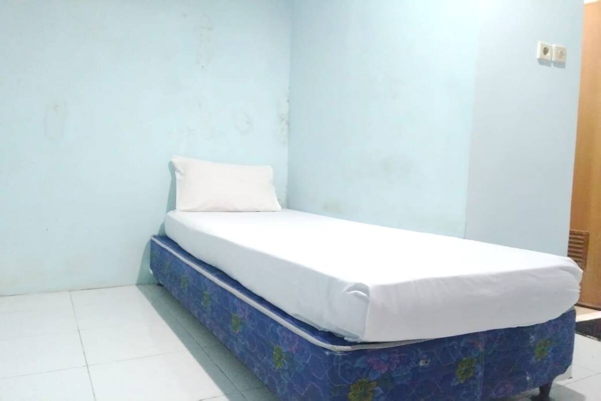 Una habitación pequeña con cama individual, cubierta con edredón azul estampado con flores y ropa de cama blanca.
