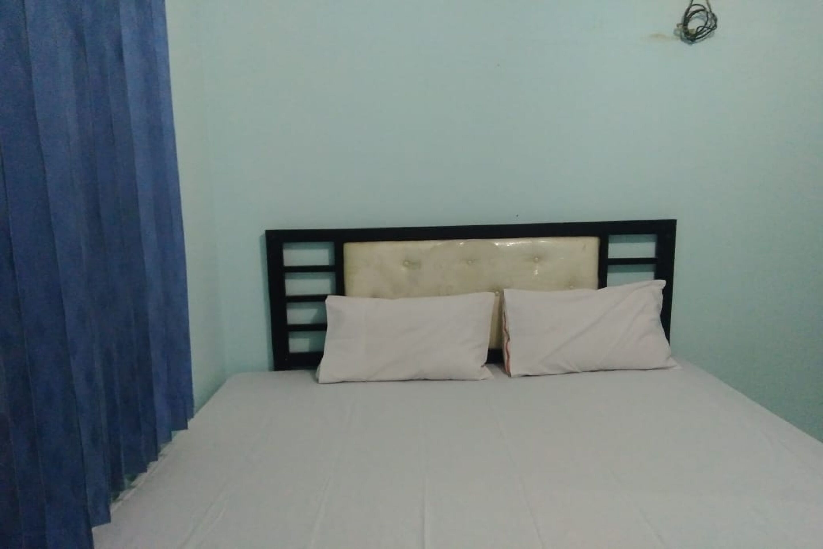 A bed with a headboard, two pillows, and a blue curtain.