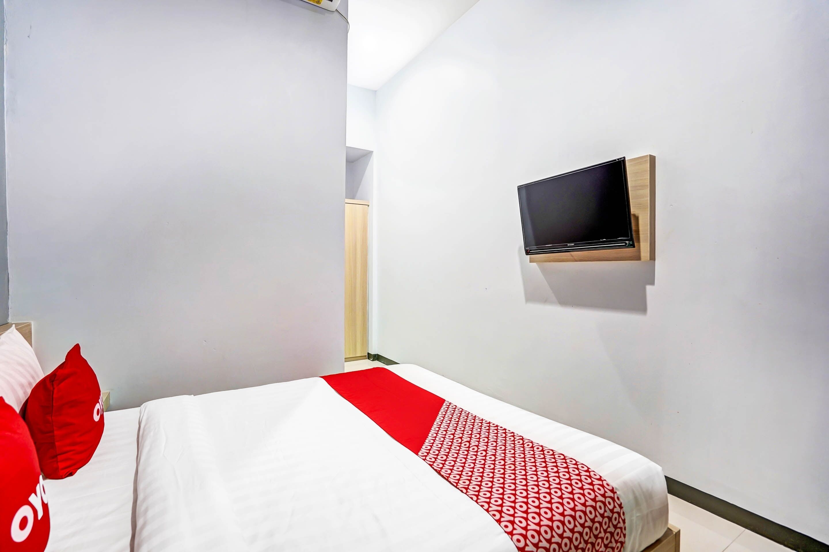 A hotel room with a bed, a TV mounted on the wall, and a door leading to a bathroom.
