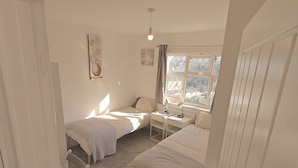 A bedroom with two beds, a desk, a chair, a radiator, and a window with curtains. - 4-bed House in Southampton Ideal For Contractors (Southampton)