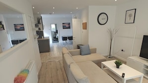 A modern living room with a sofa, a coffee table, and a TV stand. There is a staircase leading to another level. - 4-bed House in Southampton Ideal For Contractors (Southampton)