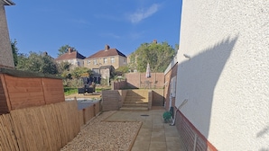 A residential backyard with a paved patio, a brick retaining wall, and a gravel area. - 4-bed House in Southampton Ideal For Contractors (Southampton)