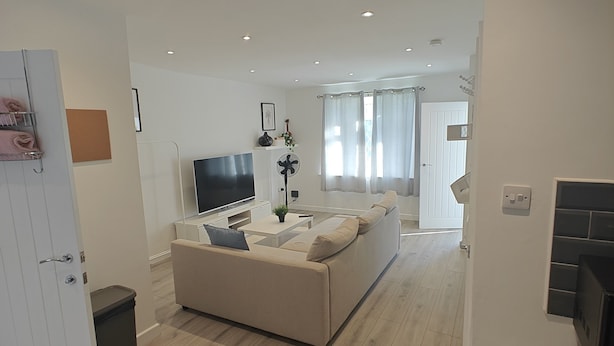 A modern living room with a sofa, TV, and a small table. - 4-bed House in Southampton Ideal For Contractors (Southampton)