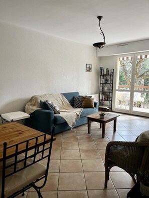 A living room with a blue sofa, a wooden coffee table, a wicker chair, and a bookshelf. - Joli Deux Pièces à Saint Raphael (Saint-Raphaël)