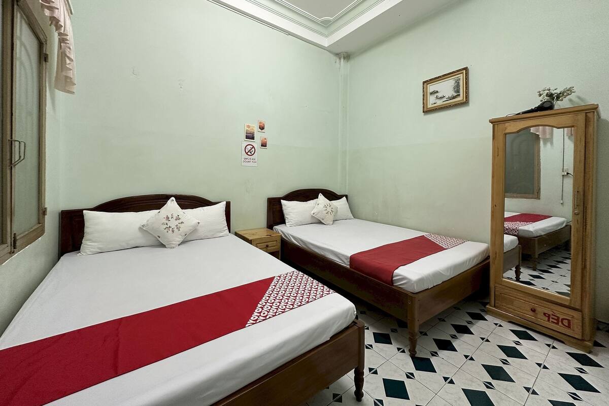 Une chambre avec deux lits simples, une armoire en bois, un miroir et un tableau accroché au mur.