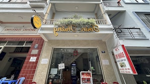 A restaurant with a sign in a foreign language, outdoor seating with plastic chairs, and a balcony with plants. - OYO 1206 Toan Thang Homestay (Xuan Huong - Da Lat)