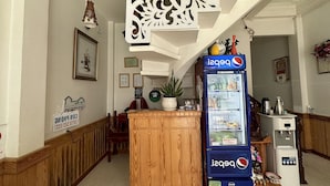 A lobby with a wooden reception desk, a Pepsi refrigerator, a water dispenser, and a decorative wall panel. - OYO 1206 Toan Thang Homestay (Xuan Huong - Da Lat)