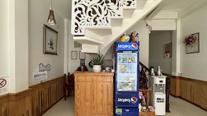 A lobby with a wooden reception desk, a Pepsi vending machine, and a trash bin. - OYO 1206 Toan Thang Homestay (Xuan Huong - Da Lat)