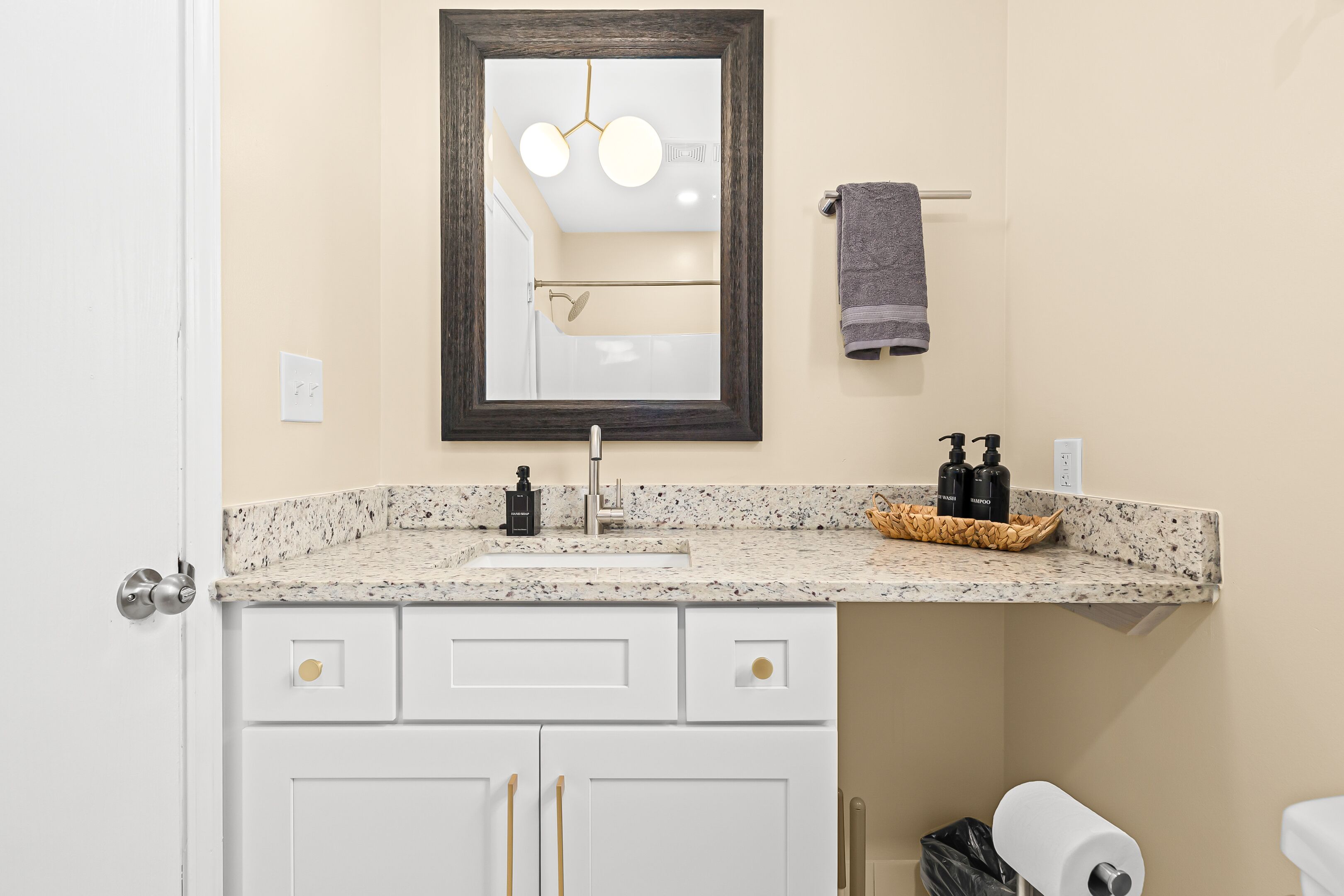 A bathroom with a white vanity, a mirror, a towel rack, and a sink with a soap dispenser.