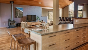 Een ruime woonkamer met een groot houten plafond, een centraal eiland met barkrukken, een open haard en een televisie.