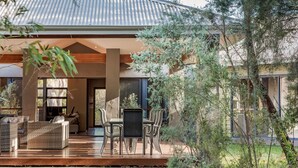 Een modern huis met een overdekt terras, tuinmeubilair en uitzicht op de omliggende begroeiing.