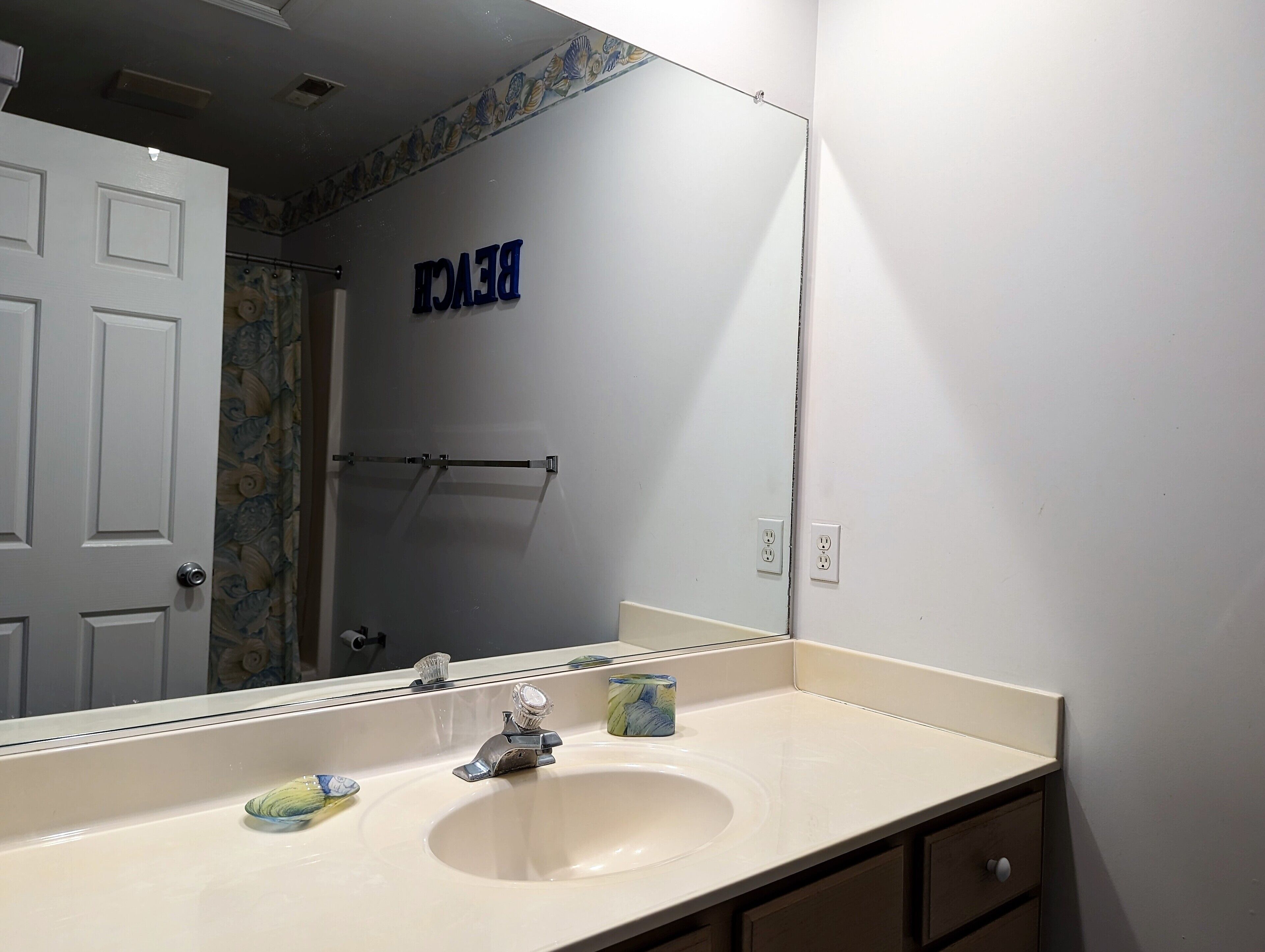 Une salle de bain équipée d’un lavabo, d’un miroir, d’un porte-serviettes et d’une porte ornée d’un motif floral.