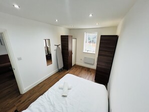 A bedroom with a bed, a mirror, a heater, and a window. - 1-bed Apartment in Ealing (London)