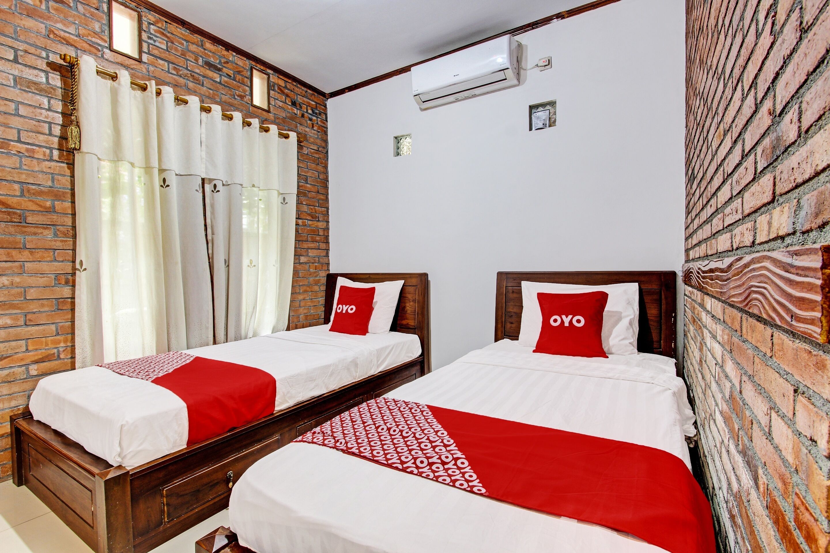 Quarto de hotel com duas camas, parede de tijolos e unidade de ar condicionado.
