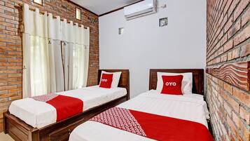 Quarto de hotel com duas camas, parede de tijolos e unidade de ar condicionado.