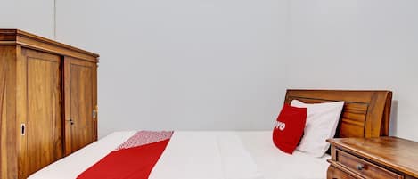 Uma cama bem arrumada com colcha vermelha e branca, uma mesinha de cabeceira de madeira e um guarda-roupa.