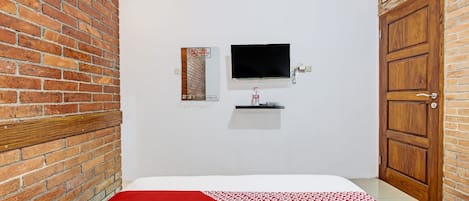 A room with a brick wall, a television mounted on the wall, a wooden door, and a bed with a red and white patterned bedspread.